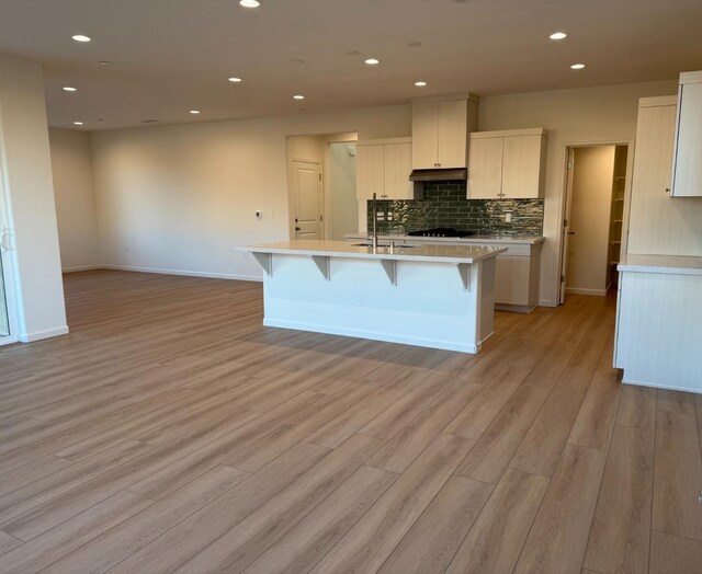 kitchen with a center island with sink, sink, light hardwood / wood-style flooring, tasteful backsplash, and a breakfast bar area