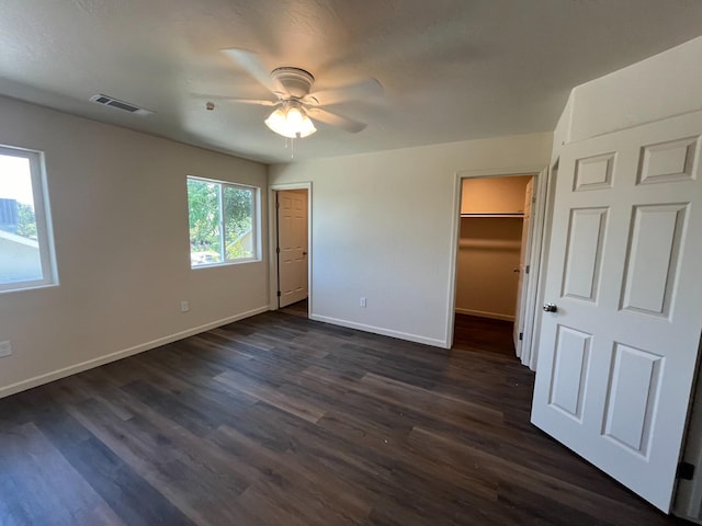 unfurnished bedroom with dark hardwood / wood-style flooring, ceiling fan, and a walk in closet