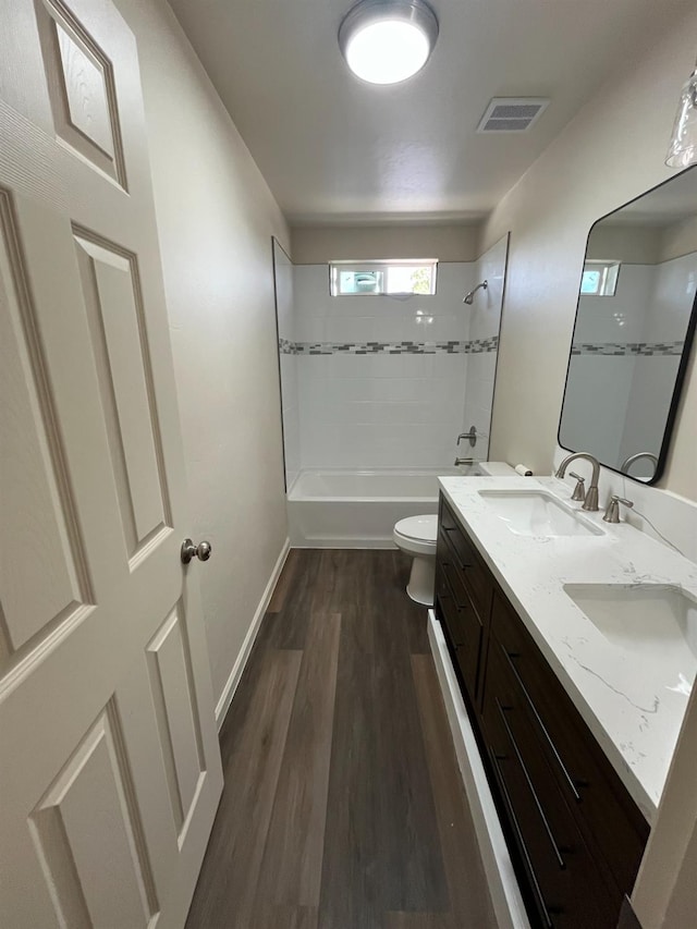 full bathroom with toilet, tiled shower / bath, hardwood / wood-style floors, and double vanity