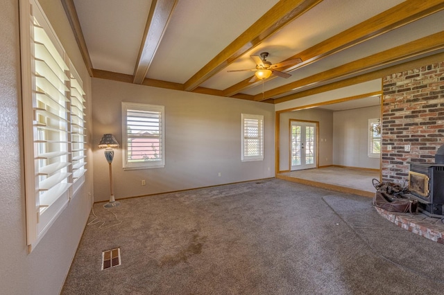 unfurnished living room featuring beamed ceiling, a wood stove, a wealth of natural light, and carpet flooring