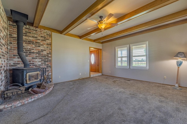 unfurnished living room featuring carpet flooring, beam ceiling, ceiling fan, and a wood stove