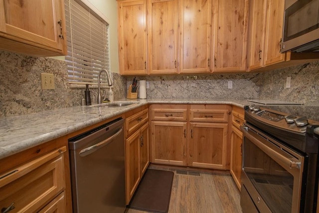 kitchen with appliances with stainless steel finishes, sink, decorative backsplash, light hardwood / wood-style floors, and light stone countertops