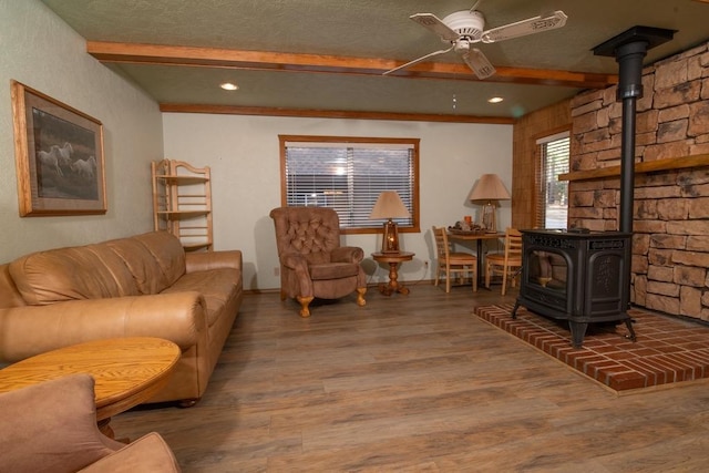 living room featuring hardwood / wood-style flooring, a wood stove, a textured ceiling, and beamed ceiling