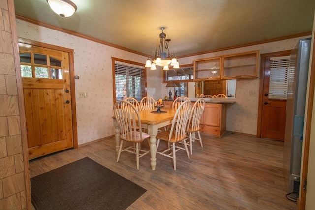 dining area featuring wood-type flooring, ornamental molding, and an inviting chandelier