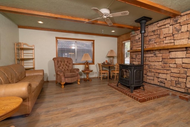 interior space with beamed ceiling, a textured ceiling, a wood stove, hardwood / wood-style flooring, and ceiling fan