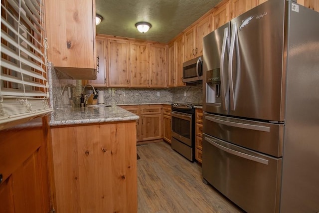 kitchen with light brown cabinetry, sink, backsplash, stainless steel appliances, and light hardwood / wood-style flooring