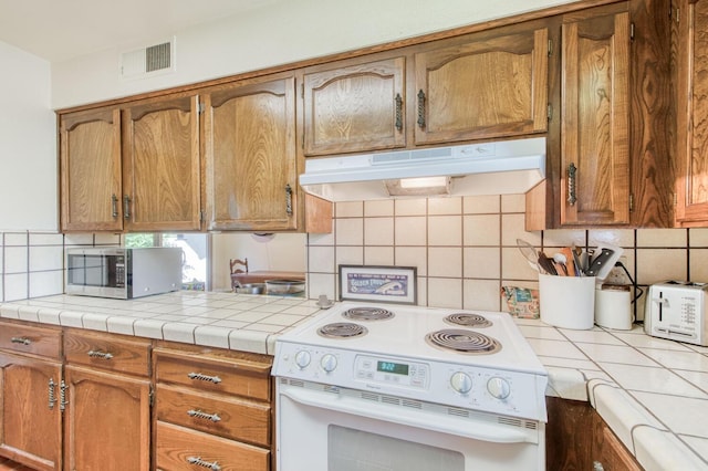 kitchen with backsplash, tile counters, custom exhaust hood, and white range oven