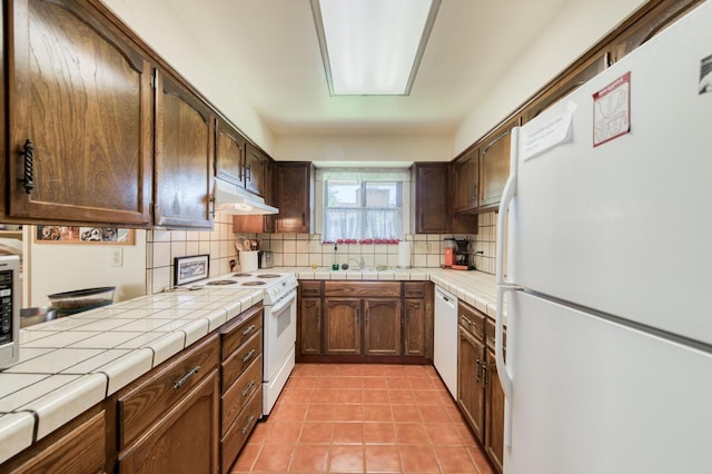 kitchen with light tile patterned flooring, decorative backsplash, white appliances, and tile countertops