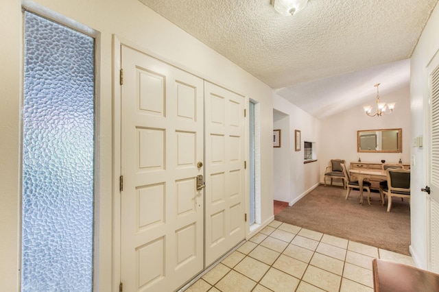 carpeted foyer entrance with a textured ceiling, a notable chandelier, and vaulted ceiling