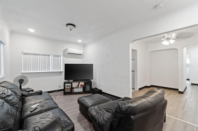 living room with light hardwood / wood-style flooring, ceiling fan, and a wall mounted air conditioner