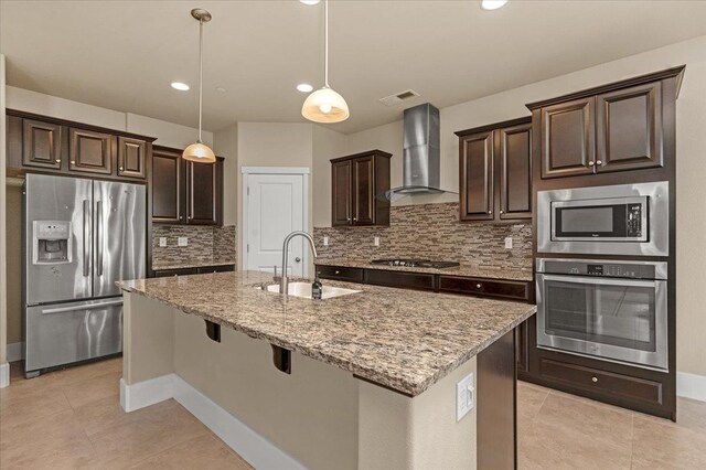 kitchen featuring appliances with stainless steel finishes, sink, decorative backsplash, an island with sink, and wall chimney exhaust hood