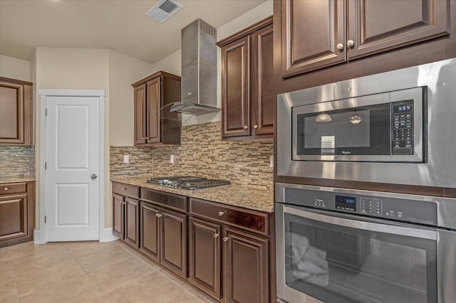 kitchen featuring tasteful backsplash, stainless steel appliances, wall chimney exhaust hood, light stone countertops, and light tile patterned floors