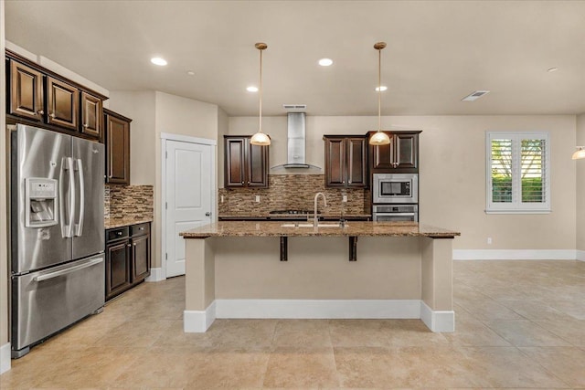 kitchen featuring stainless steel appliances, wall chimney range hood, hanging light fixtures, backsplash, and light tile patterned flooring