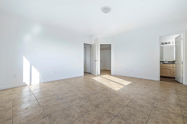 unfurnished bedroom with ensuite bathroom, a closet, light tile patterned floors, and sink