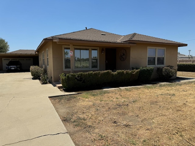 single story home featuring a shingled roof, concrete driveway, and stucco siding