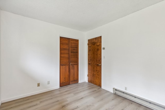 empty room featuring a baseboard heating unit, a textured ceiling, and light hardwood / wood-style flooring