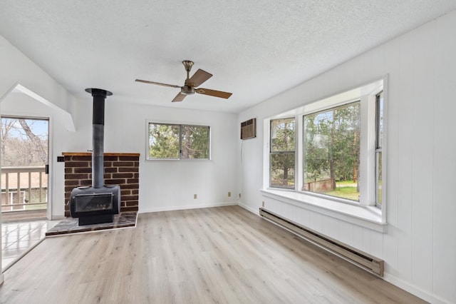 unfurnished living room featuring a healthy amount of sunlight, light wood-type flooring, a baseboard radiator, and a wood stove