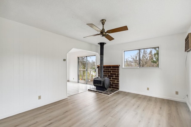 unfurnished living room featuring light hardwood / wood-style floors, a textured ceiling, a wood stove, and plenty of natural light