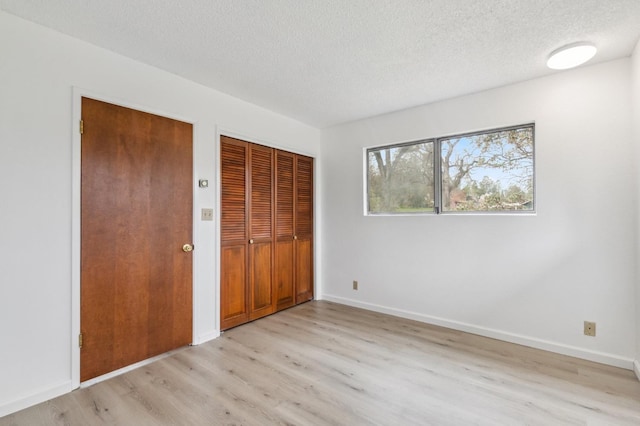 unfurnished bedroom with a textured ceiling, light hardwood / wood-style flooring, and multiple closets