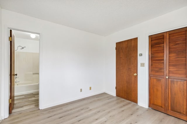 unfurnished bedroom featuring ensuite bath, a textured ceiling, and light wood-type flooring