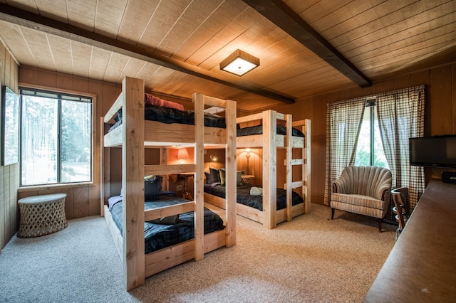 bedroom featuring wooden walls, beamed ceiling, and carpet flooring