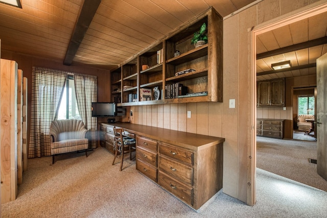 carpeted home office featuring beamed ceiling, a healthy amount of sunlight, built in desk, and wooden walls