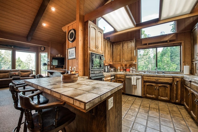 kitchen with wooden walls, tile counters, black appliances, wooden ceiling, and beam ceiling