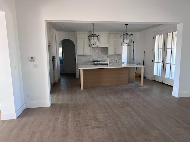 kitchen with french doors, tasteful backsplash, pendant lighting, hardwood / wood-style flooring, and a center island with sink