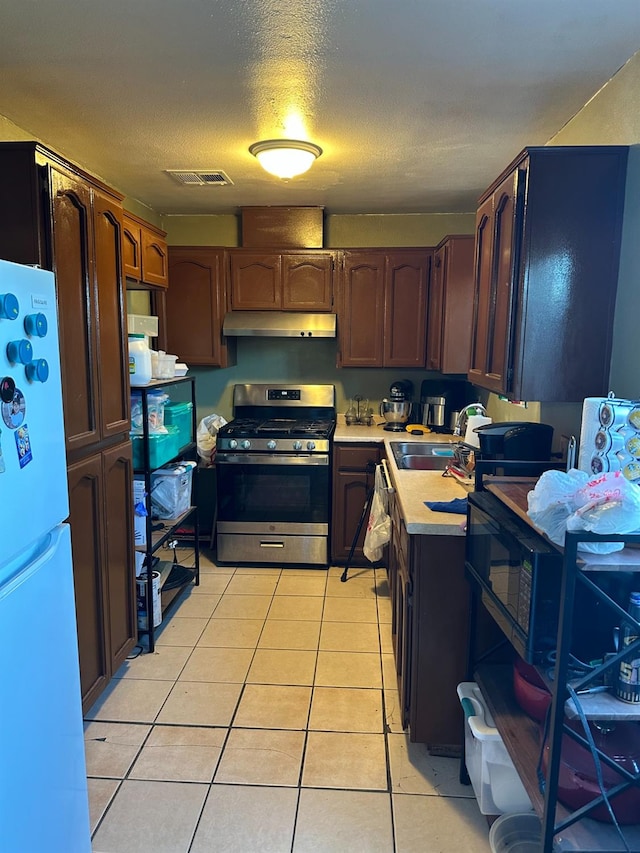 kitchen featuring sink, gas range, a textured ceiling, light tile patterned floors, and white fridge