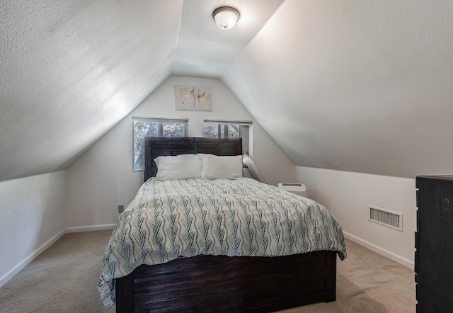 bedroom with a textured ceiling, lofted ceiling, light carpet, visible vents, and baseboards