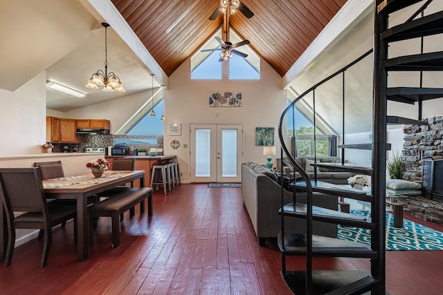 dining room featuring high vaulted ceiling, a stone fireplace, ceiling fan with notable chandelier, french doors, and dark wood finished floors