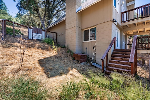 view of side of home featuring stairway, a chimney, concrete block siding, and fence