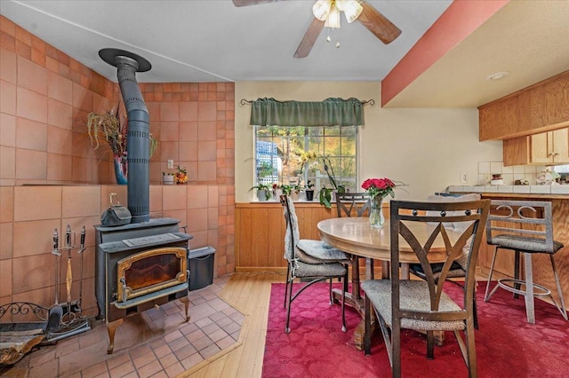 dining room featuring a wood stove, hardwood / wood-style floors, tile walls, and ceiling fan