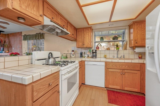 kitchen with tile counters, sink, light wood-type flooring, white appliances, and tasteful backsplash