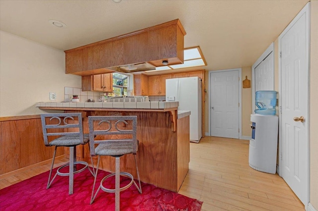 kitchen featuring kitchen peninsula, a breakfast bar, white refrigerator with ice dispenser, light hardwood / wood-style floors, and tasteful backsplash