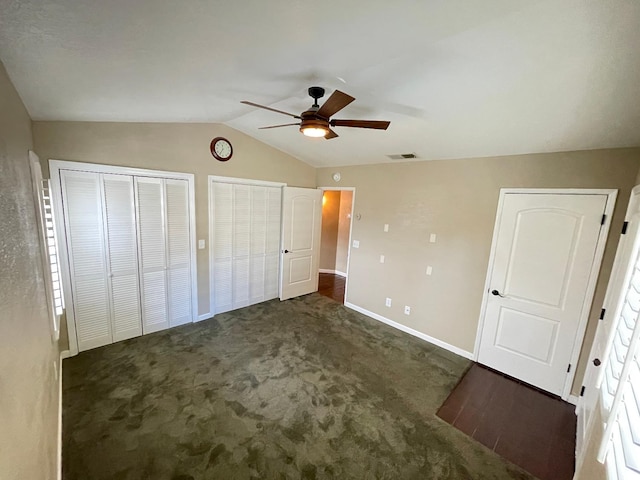 unfurnished bedroom featuring ceiling fan, multiple closets, vaulted ceiling, and dark colored carpet