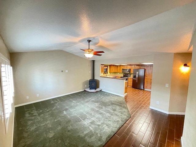 unfurnished living room with a wood stove, vaulted ceiling, dark hardwood / wood-style flooring, a textured ceiling, and ceiling fan