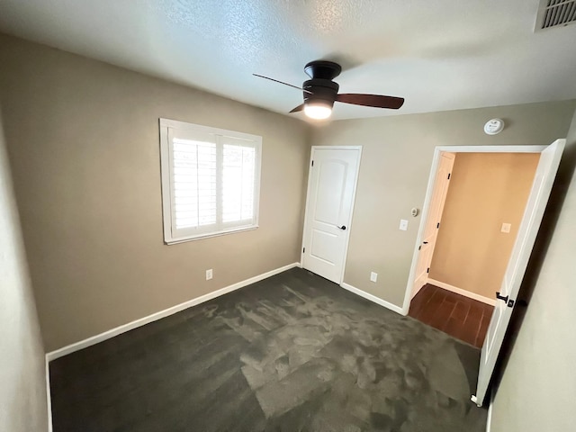 unfurnished bedroom with ceiling fan, a textured ceiling, and dark carpet