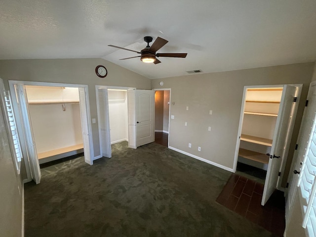 unfurnished bedroom featuring ceiling fan, multiple closets, vaulted ceiling, and dark carpet