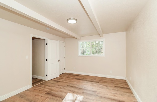 unfurnished bedroom featuring beamed ceiling and light hardwood / wood-style floors