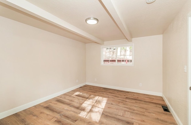 unfurnished room with a textured ceiling, beam ceiling, and light wood-type flooring