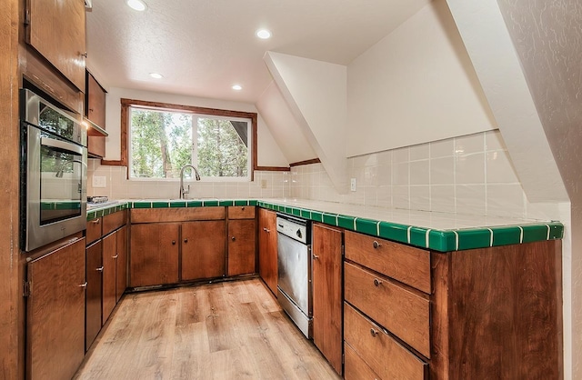 kitchen with tasteful backsplash, light wood-type flooring, appliances with stainless steel finishes, vaulted ceiling, and tile countertops