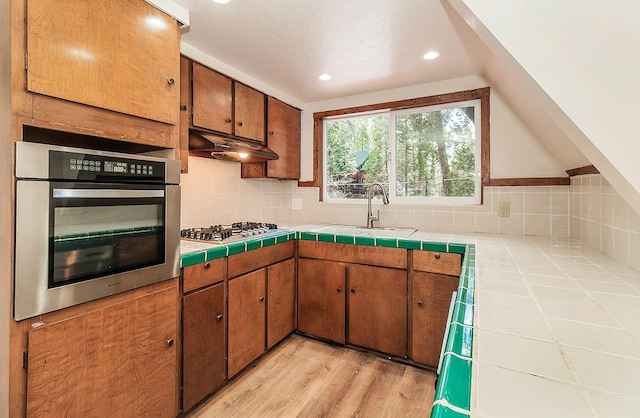 kitchen with backsplash, tile counters, light wood-type flooring, and stainless steel appliances