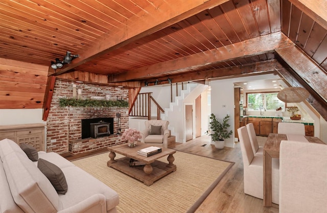 living room featuring beamed ceiling, wood ceiling, sink, light wood-type flooring, and a brick fireplace