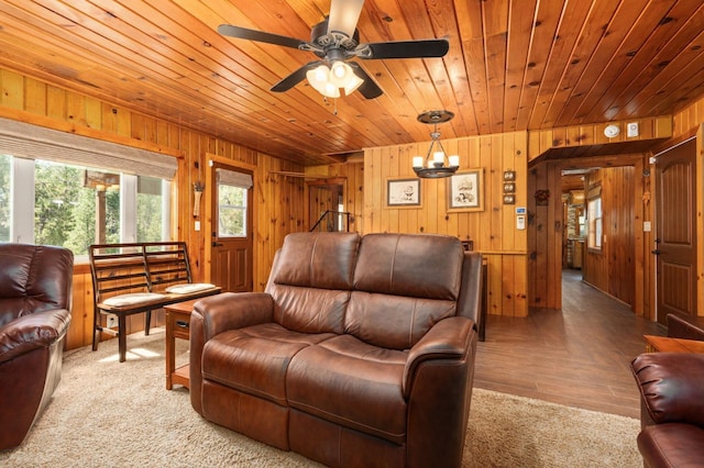 living room with ceiling fan with notable chandelier, wooden ceiling, and wood walls