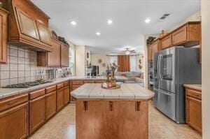 kitchen with tile counters, gas stovetop, a kitchen breakfast bar, stainless steel fridge, and a kitchen island