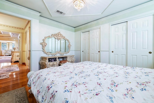 bedroom featuring a notable chandelier, crown molding, multiple closets, and hardwood / wood-style flooring