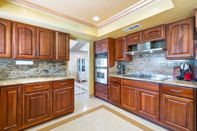 kitchen featuring wall chimney exhaust hood, black electric stovetop, a tray ceiling, and light stone countertops