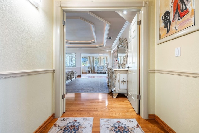 hall featuring ornamental molding, a tray ceiling, and light wood-type flooring