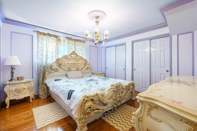 bedroom with multiple closets, crown molding, hardwood / wood-style flooring, and an inviting chandelier